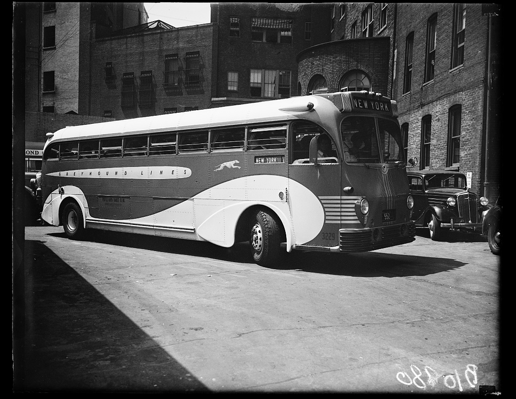 A black and white photograph of a bus turning around the corner.