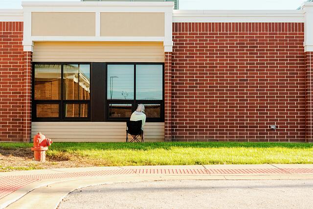 Woman sitting on a folding chair looking into a window of a brick building